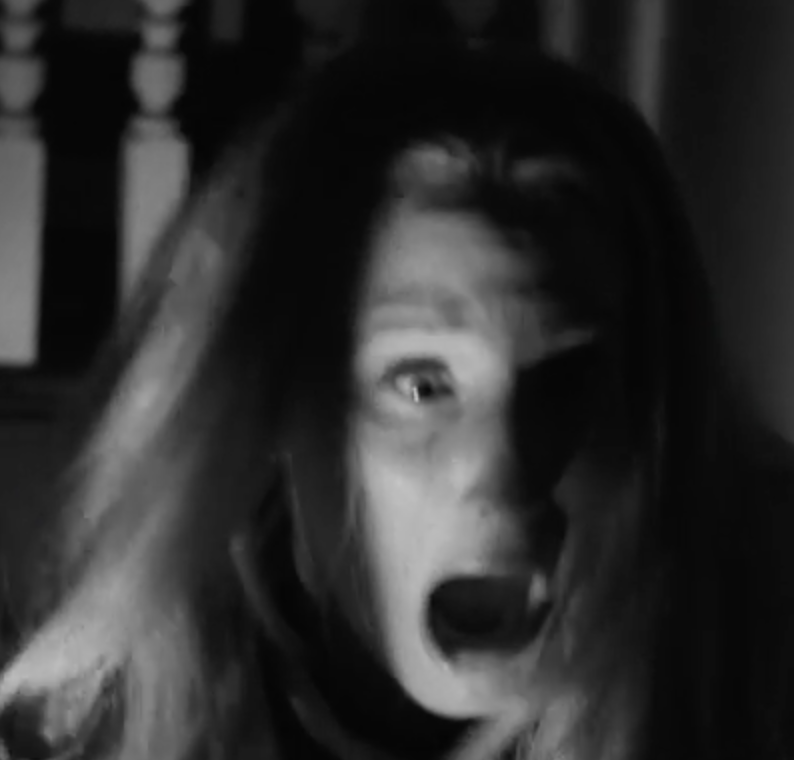 A woman looks off screen with a frightened expression in a black-and-white close-up.